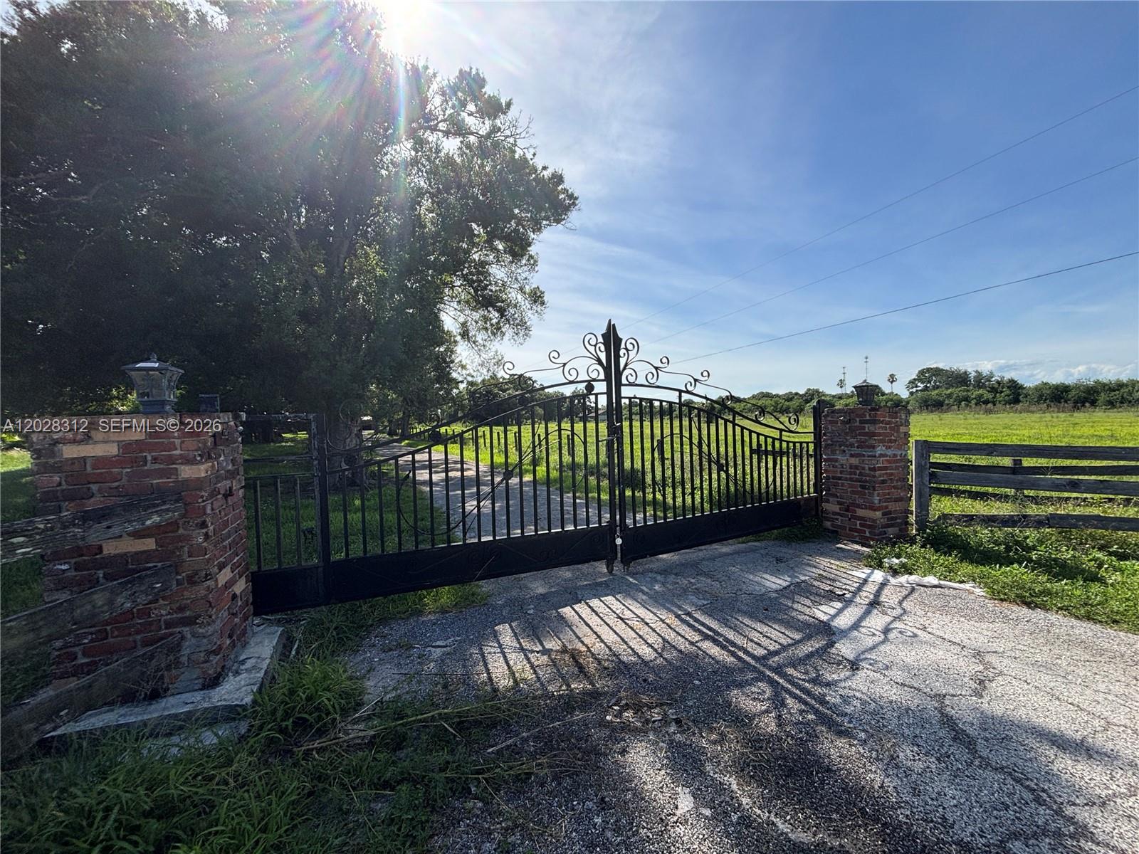 A black wrought iron gate is mounted between two brick pillars at a property entrance — 375 & 311 County Road 720, Clewiston FL 33440, CLEWISTON, FL
