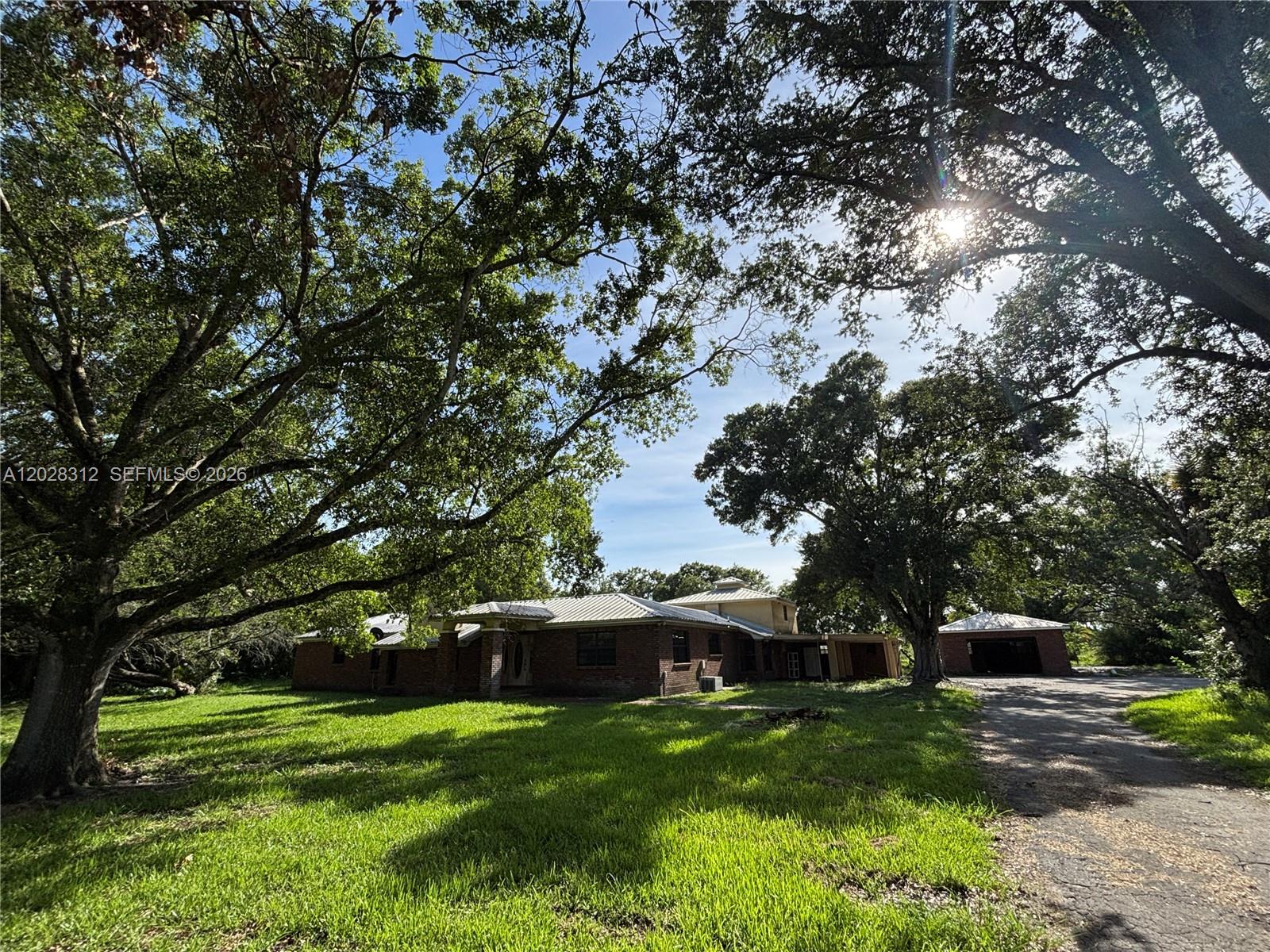 A brick house with a metal roof sits on a grassy lot with large trees — 375 & 311 County Road 720, Clewiston FL 33440, CLEWISTON, FL