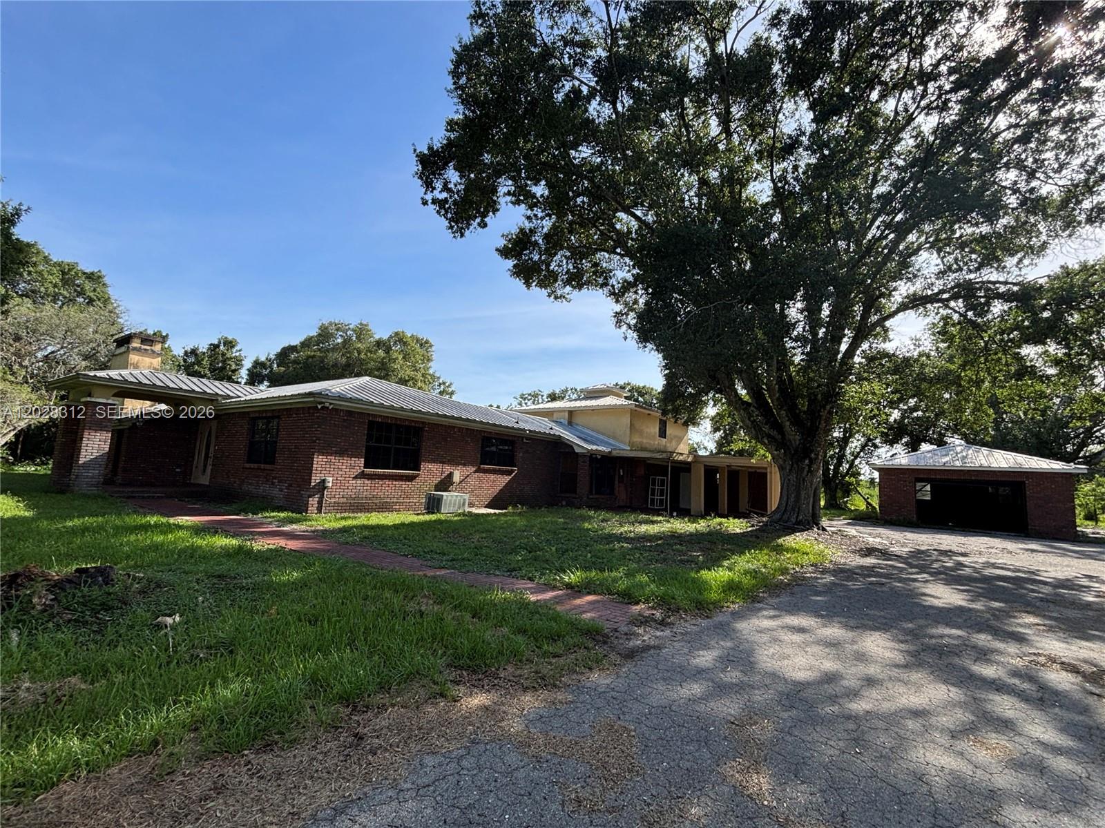 A brick house with a metal roof stands next to a detached garage and tree — 375 & 311 County Road 720, Clewiston FL 33440, CLEWISTON, FL
