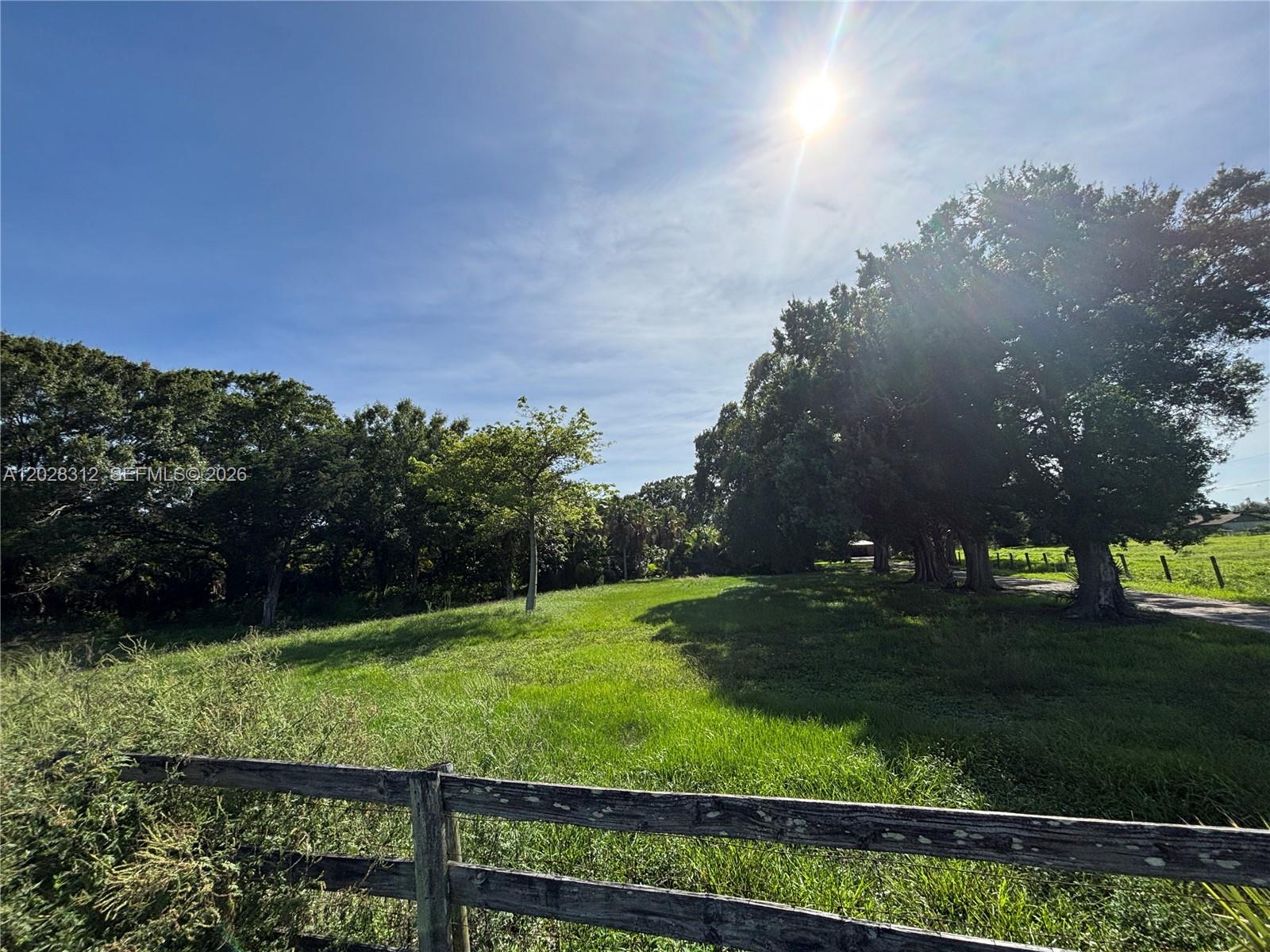 A wooden fence borders a grassy field with mature trees under a bright sun — 375 & 311 County Road 720, Clewiston FL 33440, CLEWISTON, FL