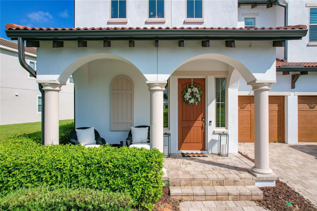 A covered front porch features arched openings, two chairs, and a wooden front door — 8216 TOPSAIL PLACE, WINTER GARDEN, FL