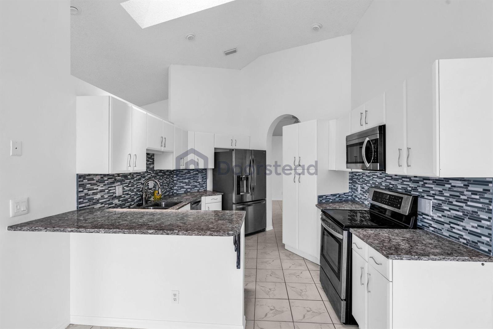 A kitchen features white cabinets, granite countertops, a tiled backsplash, and stainless steel appliances — 12382 Pleasant Green Way, Boynton Beach FL 33437, BOYNTON BEACH, FL