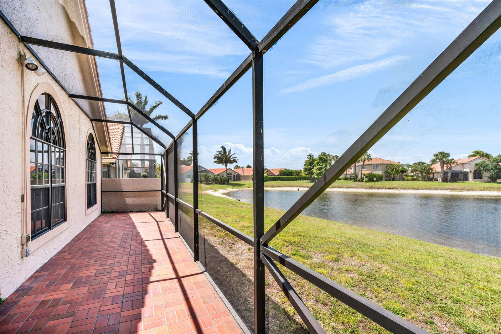 A screened-in brick patio overlooks a pond and residential neighborhood on a sunny day — 12382 Pleasant Green Way, Boynton Beach FL 33437, BOYNTON BEACH, FL