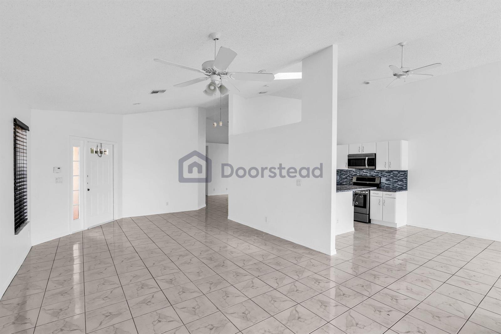 This open-concept living area features white walls, tiled floors, ceiling fans, and an adjacent kitchen — 12382 Pleasant Green Way, Boynton Beach FL 33437, BOYNTON BEACH, FL