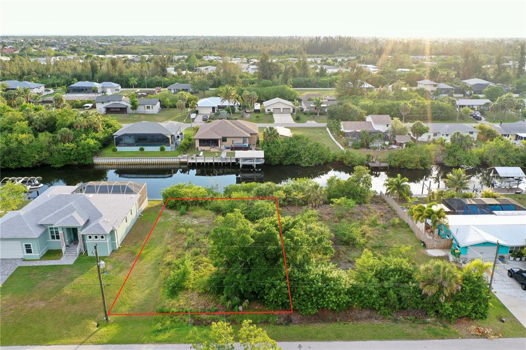 An aerial view shows a vacant, tree-covered residential lot outlined in red along a canal — 3717 WISTERIA PLACE, PUNTA GORDA, FL
