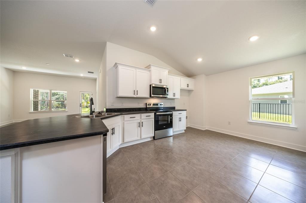 A kitchen features white cabinets, dark countertops, stainless steel appliances, and tile flooring — 77 PICKERING DRIVE, PALM COAST, FL