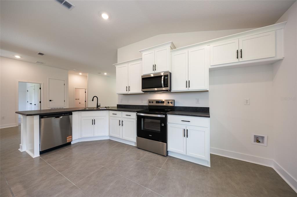A modern kitchen features white cabinets, stainless steel appliances, and dark countertops on gray tile — 77 PICKERING DRIVE, PALM COAST, FL