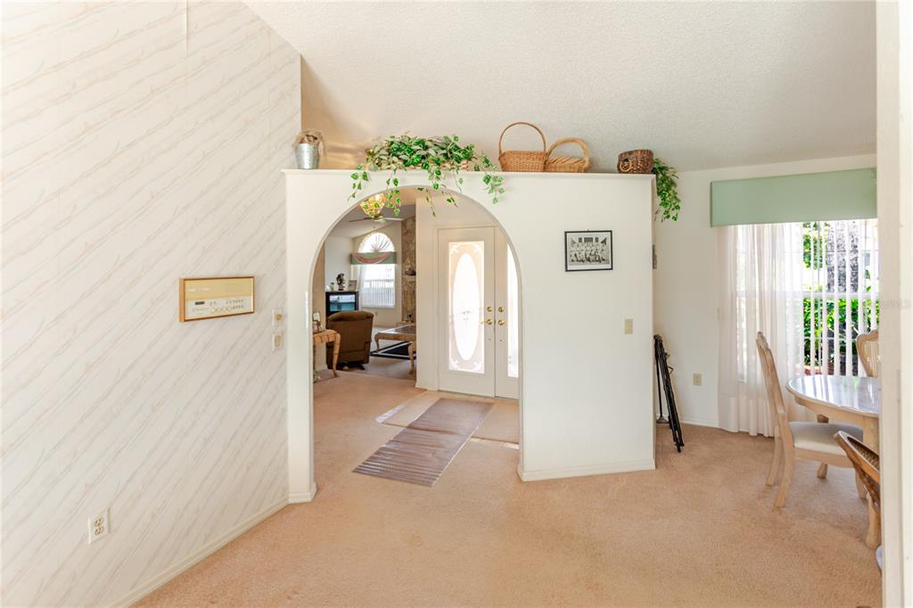 A carpeted dining area features an arched entryway leading to a living room with glass doors — 11034 AUBURNDALE STREET, SPRING HILL, FL
