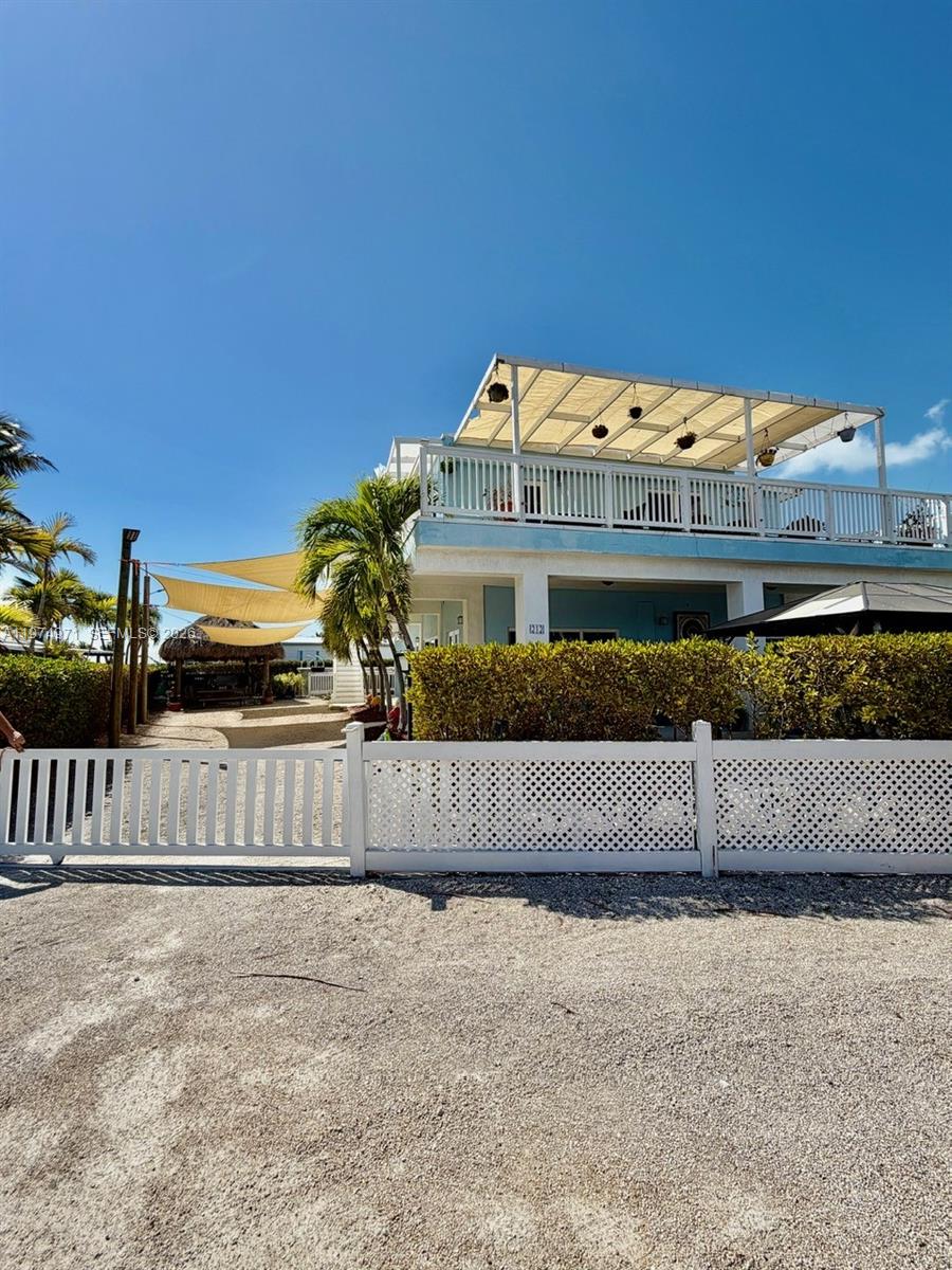 A two-story house with a white lattice fence and a large rooftop canopy — 212 Banyan Ln, Tavernier FL 33070, TAVERNIER, FL