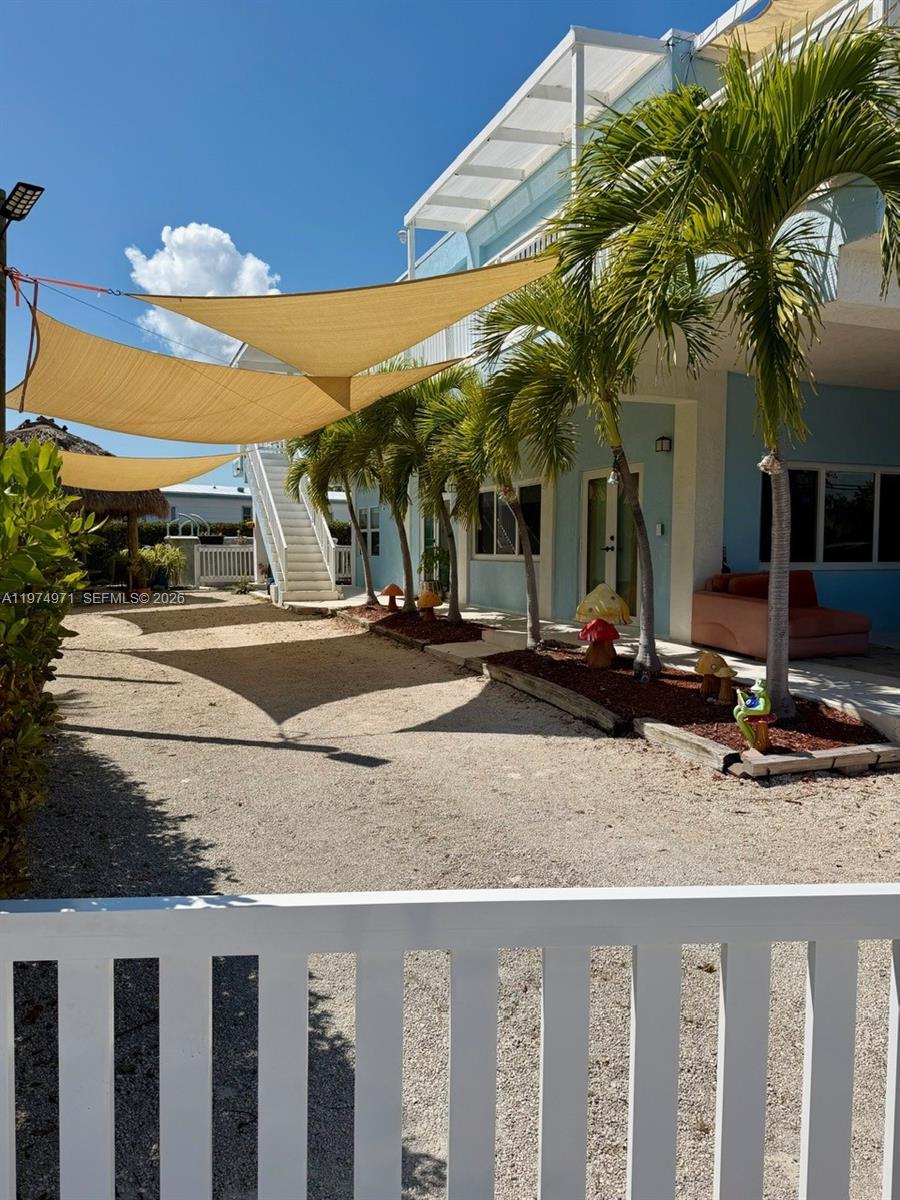 A gravel yard with shade sails, palm trees, and a staircase leading to a building — 212 Banyan Ln, Tavernier FL 33070, TAVERNIER, FL