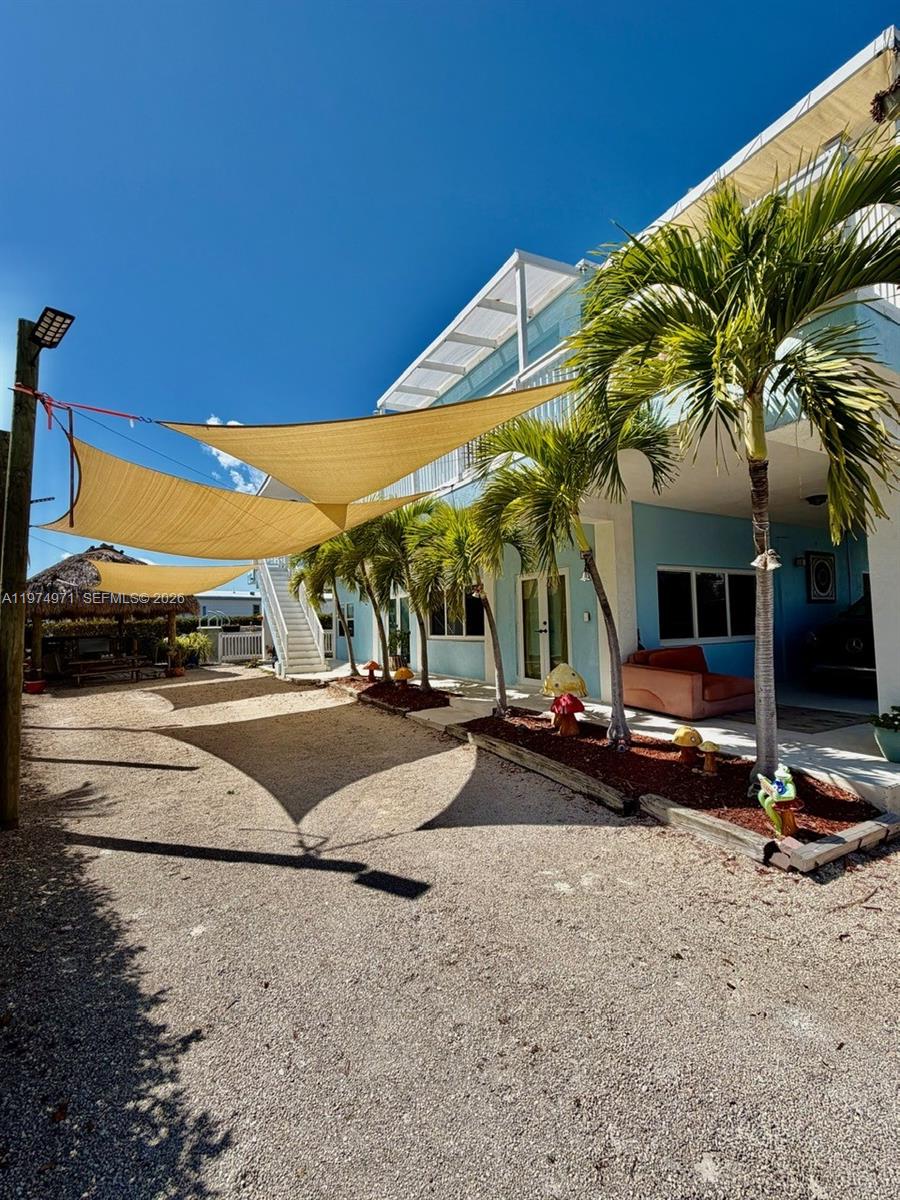 A gravel yard features shade sails, palm trees, and a multi-story light blue house — 212 Banyan Ln, Tavernier FL 33070, TAVERNIER, FL
