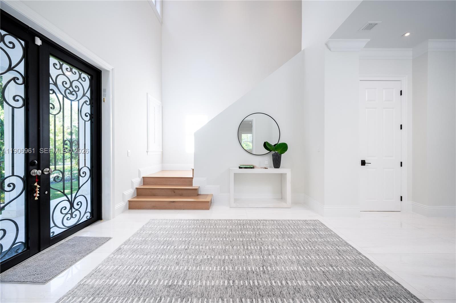 A bright entryway features white walls, tile floors, a wooden staircase, and a black door — 680 Destacada Ave, Coral Gables FL 33156, CORAL GABLES, FL
