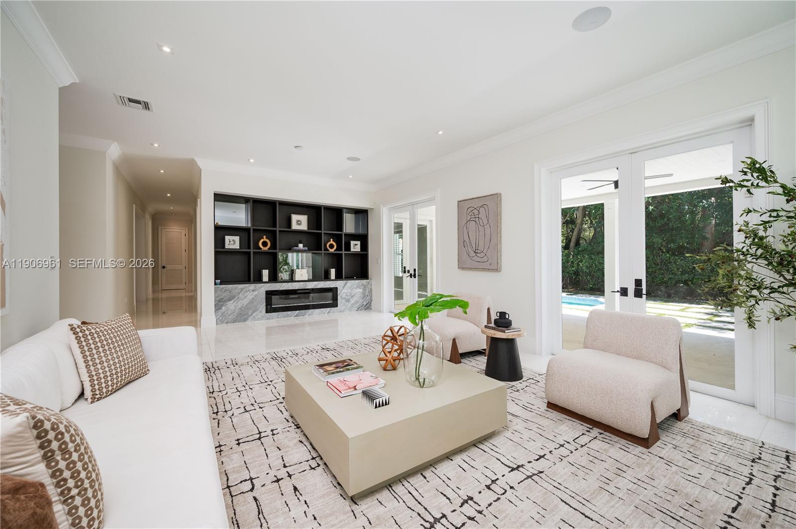 A modern living room features a marble fireplace, built-in shelving, and glass doors to a patio — 680 Destacada Ave, Coral Gables FL 33156, CORAL GABLES, FL