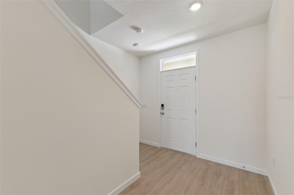 An entryway features light wood-look flooring, a white front door, and a staircase — 3038 HOUSE FINCH ROAD, ST CLOUD, FL