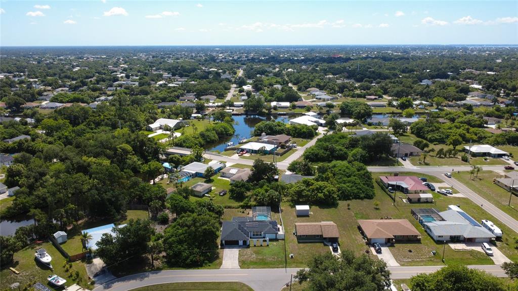 An aerial view shows a residential neighborhood with houses, green trees, and a small canal — 2772 AUBURN BOULEVARD, PORT CHARLOTTE, FL