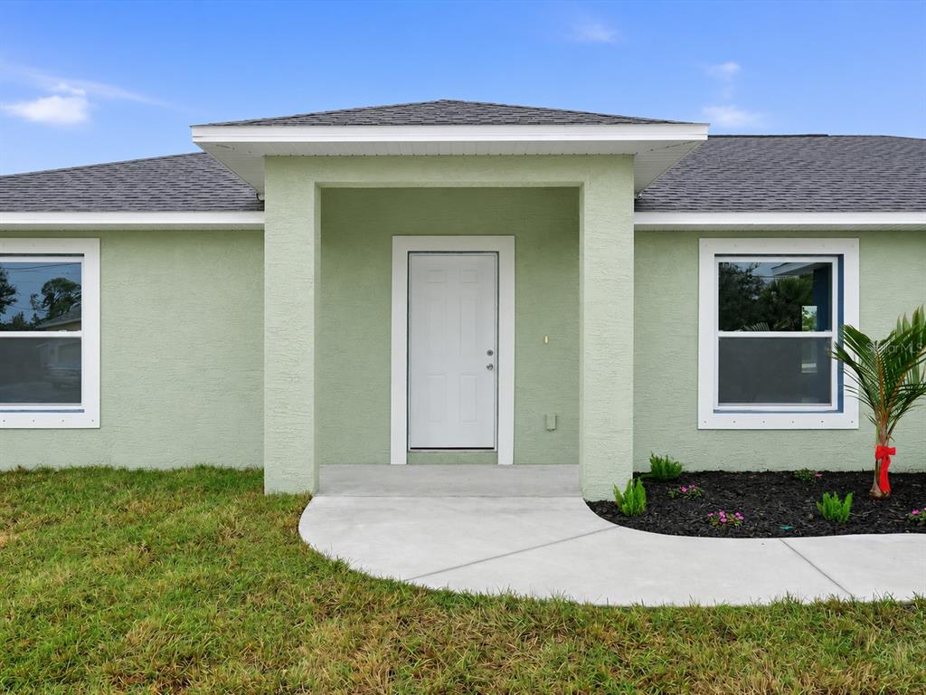 A light green house exterior features a white front door under a covered entryway — 12081 SNOW BIRD AVENUE, PORT CHARLOTTE, FL