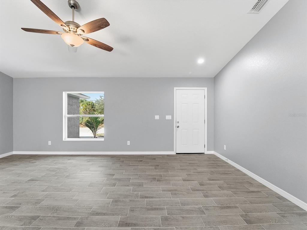 An empty room features gray walls, wood-look tile flooring, a ceiling fan, and a door — 12081 SNOW BIRD AVENUE, PORT CHARLOTTE, FL