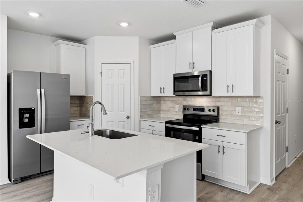A modern kitchen features white cabinets, stainless steel appliances, a quartz island, and tile backsplash — 16278 BIRD OF PARADISE AVENUE, CLERMONT, FL