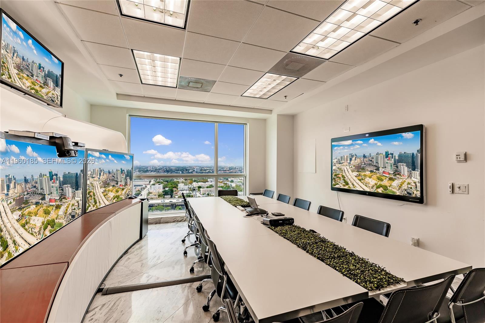 A modern conference room features a long table, multiple wall-mounted screens, and city views — 175 SW 7th St # 1901, Miami FL 33130, MIAMI, FL