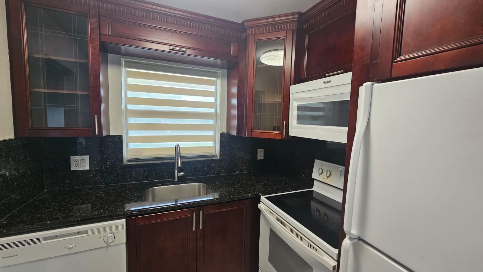 A kitchen featuring dark wood cabinets, black granite countertops, and white appliances — 9911 Sandalfoot Boulevard # 116, Boca Raton FL 33428, BOCA RATON, FL