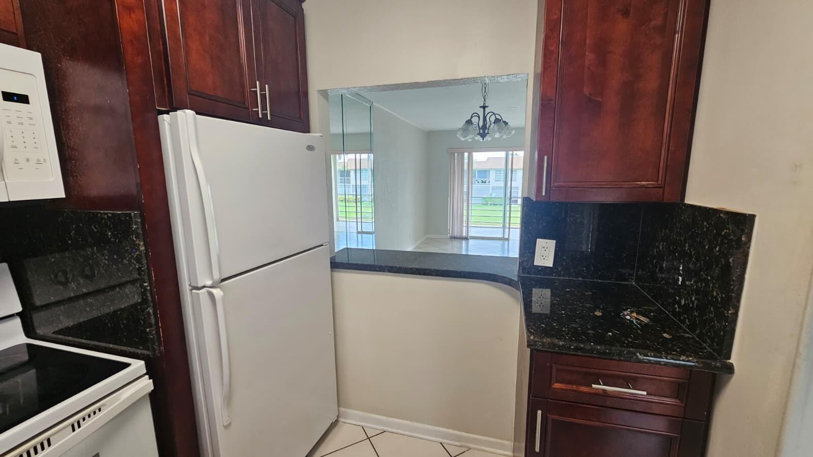 A kitchen with dark wood cabinets, black granite countertops, and a pass-through window to the dining area — 9911 Sandalfoot Boulevard # 116, Boca Raton FL 33428, BOCA RATON, FL