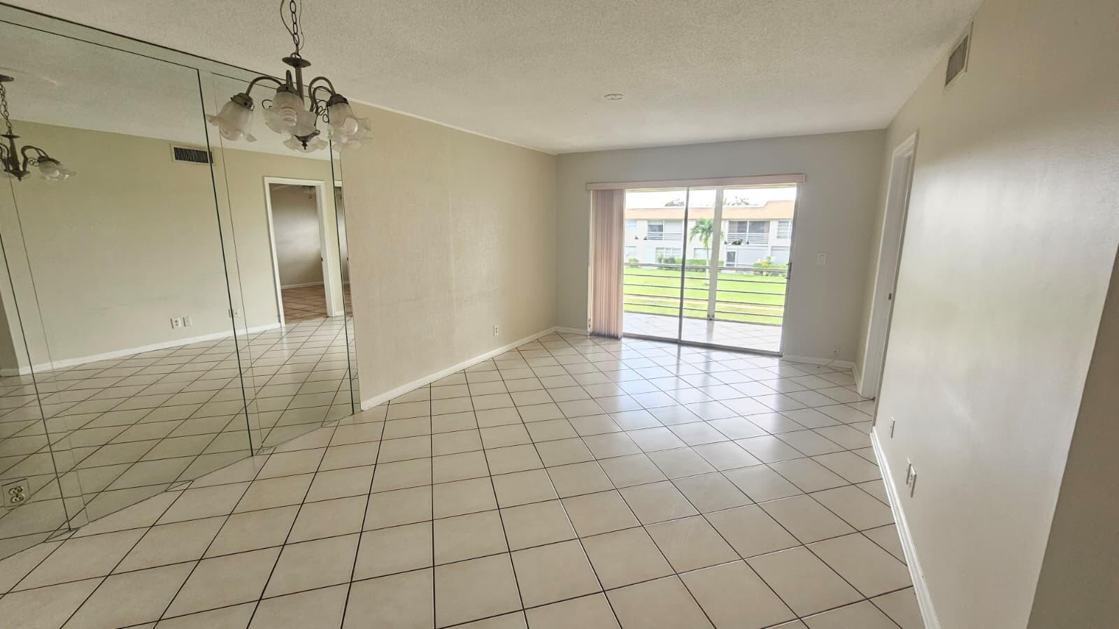 A living room with beige tile floors, a mirrored wall, and a sliding glass door — 9911 Sandalfoot Boulevard # 116, Boca Raton FL 33428, BOCA RATON, FL