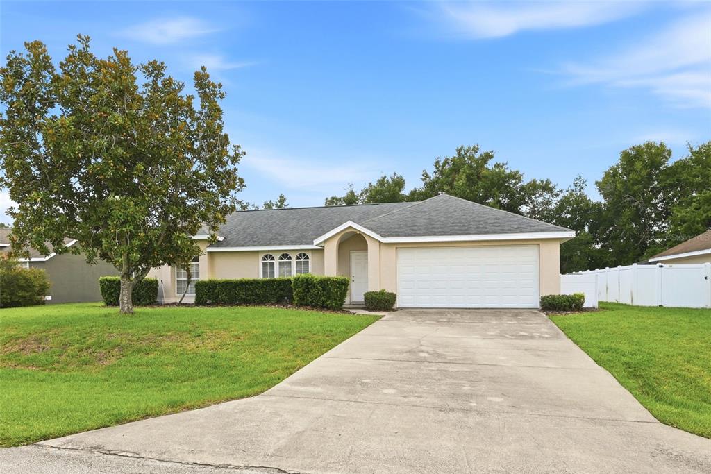 A single-story house with a beige exterior, a two-car garage, and a large front tree — 143 WHITEHALL STREET, DAVENPORT, FL