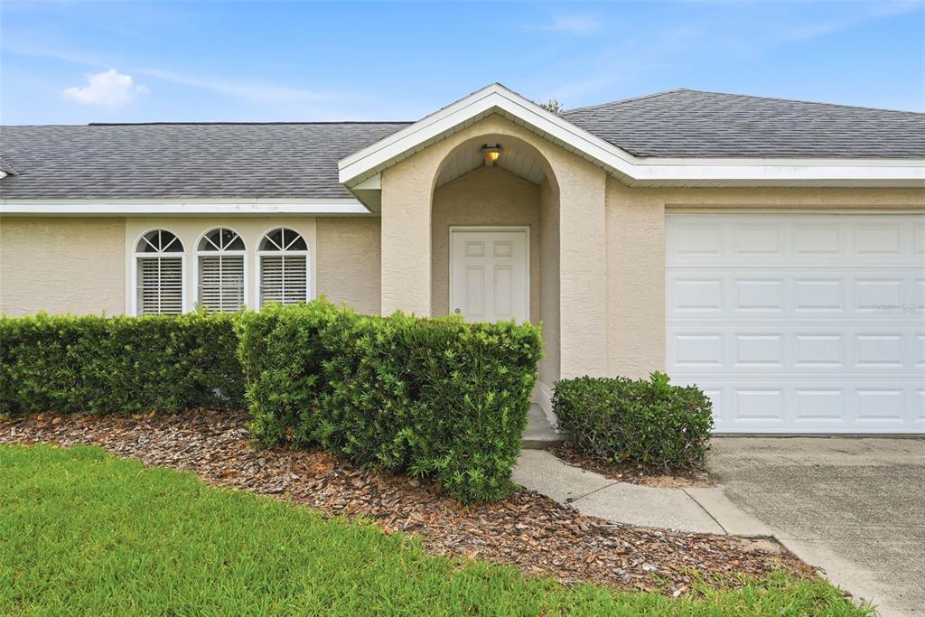 The exterior of a single-story house features a white garage door and arched entryway — 143 WHITEHALL STREET, DAVENPORT, FL