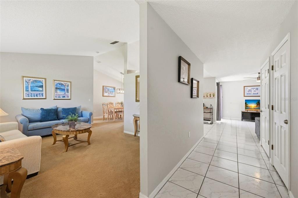 A living room with carpeted floors and a tiled hallway leading to a family room — 143 WHITEHALL STREET, DAVENPORT, FL