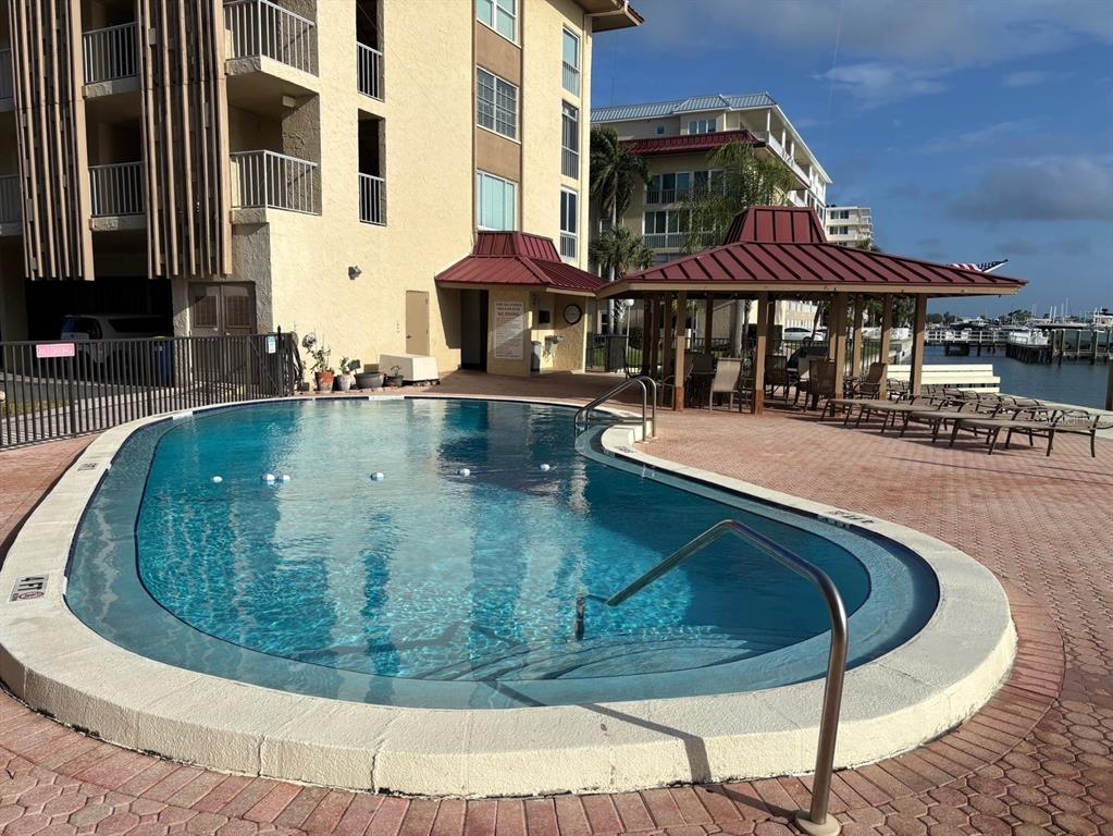 A swimming pool with a metal handrail sits on a brick patio beside a building — 121 ISLAND WAY UNIT 331, CLEARWATER BEACH, FL