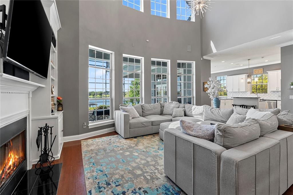 A living room with a fireplace, large sectional sofa, and tall windows overlooking a lake — 9648 WEATHERSTONE COURT, WINDERMERE, FL