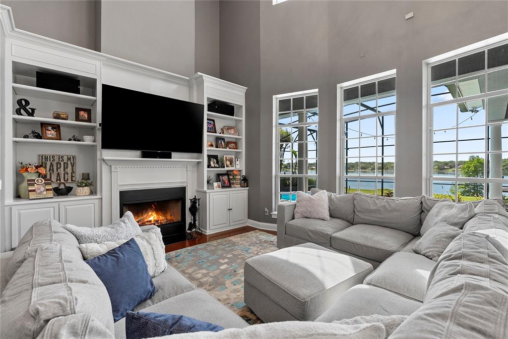 A living room features a fireplace, built-in shelving, a sectional sofa, and large windows — 9648 WEATHERSTONE COURT, WINDERMERE, FL