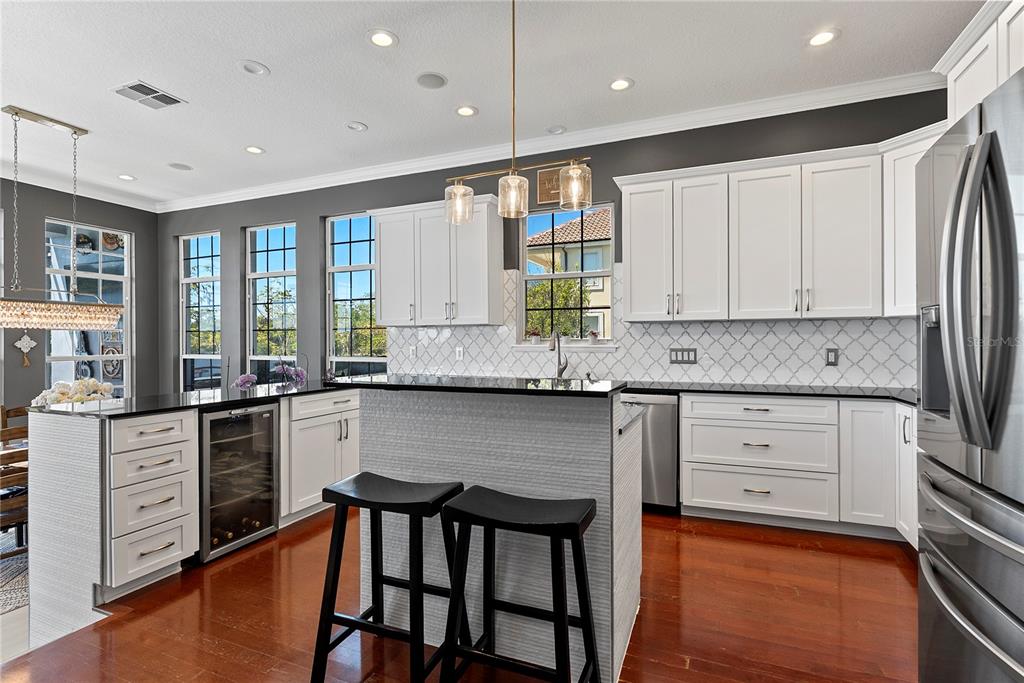 A kitchen features white cabinets, black countertops, a central island with bar stools, and windows — 9648 WEATHERSTONE COURT, WINDERMERE, FL