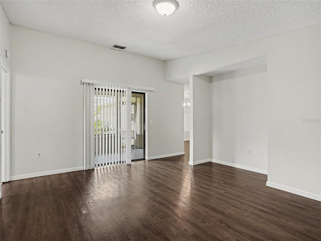 An empty room with dark wood-look flooring, white walls, and a sliding glass door — 406 LAKE DAISY DRIVE, WINTER HAVEN, FL