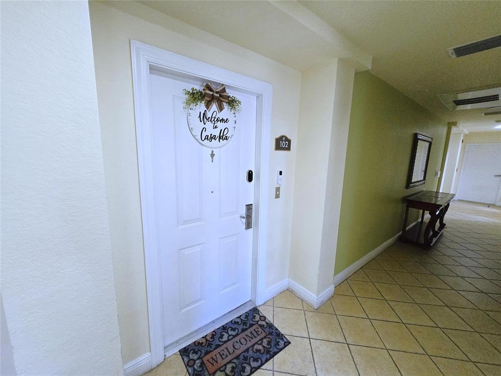 A white front door with a welcome sign and mat leads into a tiled hallway — 1322 SEVEN EAGLES COURT UNIT 102, REUNION, FL