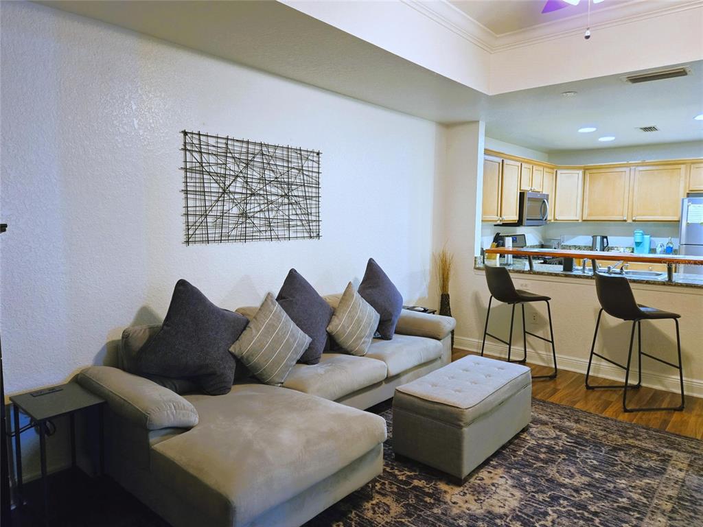 A living room with a sectional sofa and ottoman opens to a kitchen with bar seating — 1322 SEVEN EAGLES COURT UNIT 102, REUNION, FL
