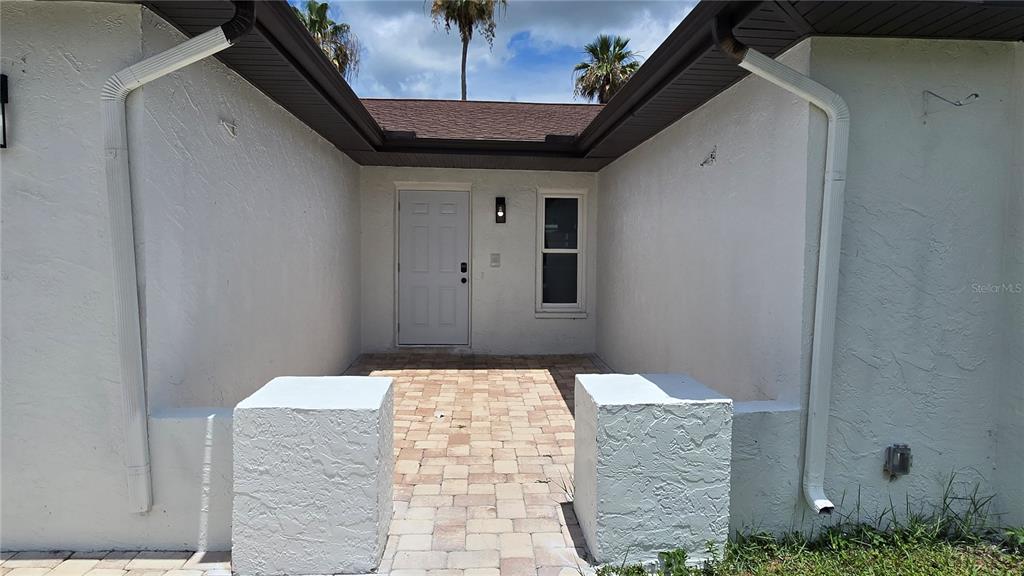 A paved entryway leads to a white front door flanked by two stucco pillars — 8607 LONGBOAT LANE, HUDSON, FL