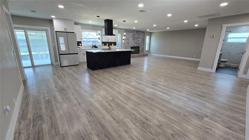 A modern open-concept kitchen and living area features light wood flooring and a brick fireplace — 8607 LONGBOAT LANE, HUDSON, FL