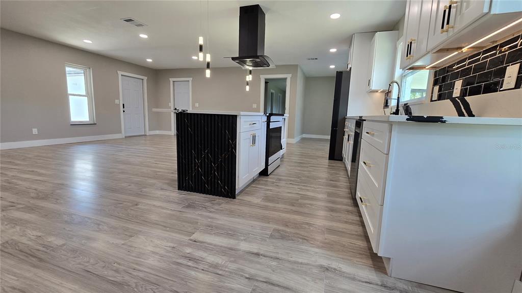 A modern kitchen features white cabinets, a black range hood, and a central island — 8607 LONGBOAT LANE, HUDSON, FL