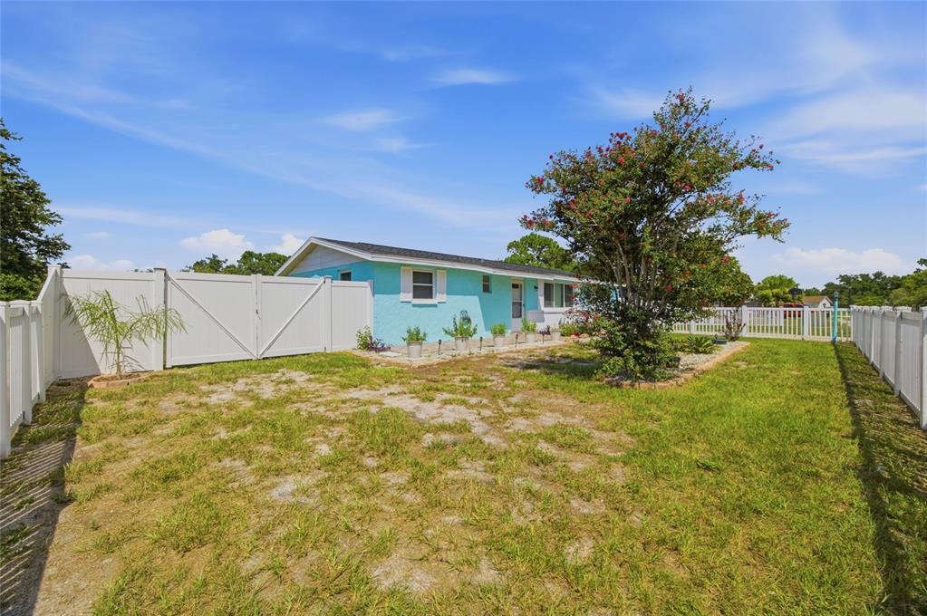 A light blue house with white trim sits behind a white vinyl fence — 9347 MIRACLE DRIVE, SPRING HILL, FL