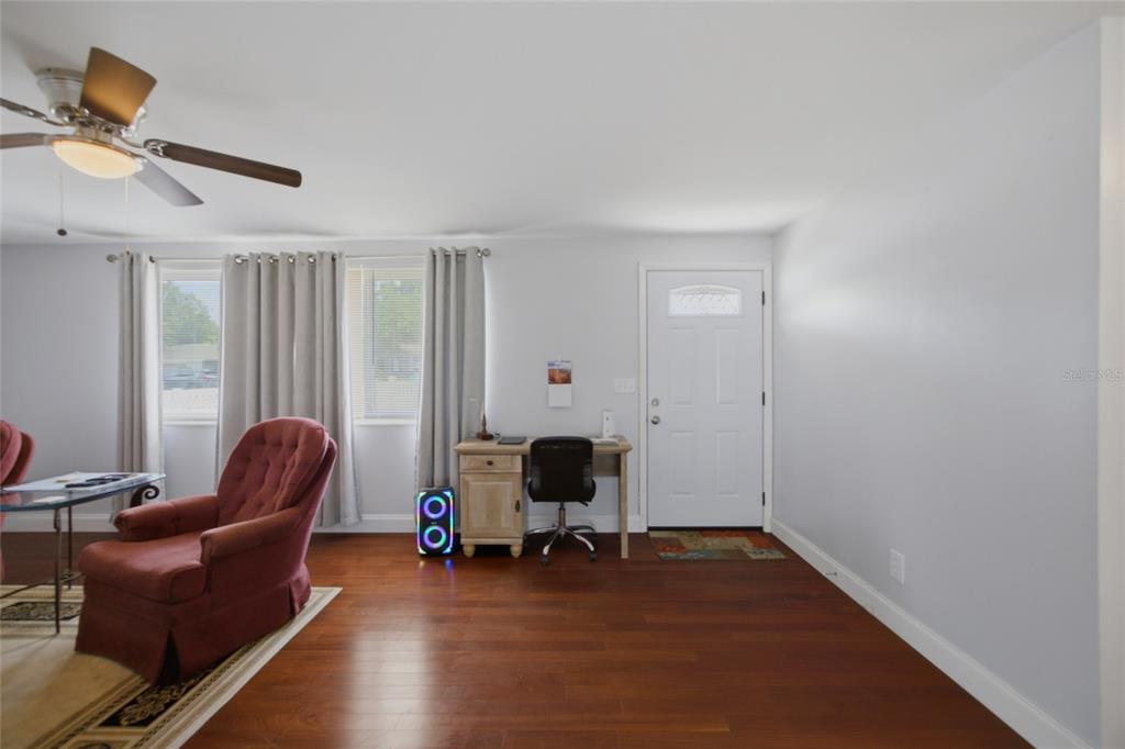 A living room with hardwood floors, a desk, a red armchair, and a front door — 9347 MIRACLE DRIVE, SPRING HILL, FL