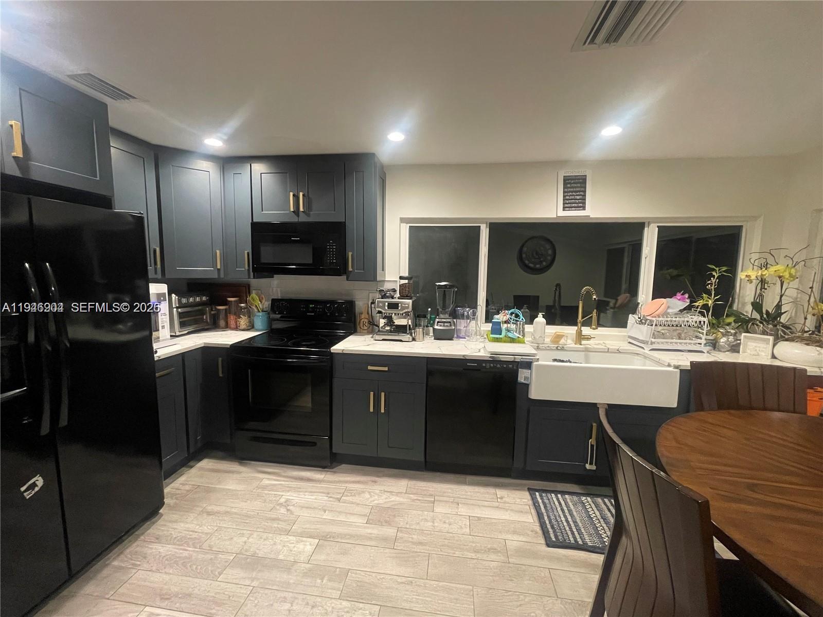 A kitchen features dark blue cabinets, black appliances, a farmhouse sink, and light-colored countertops — 2730 Adams St, Hollywood FL 33020, HOLLYWOOD, FL