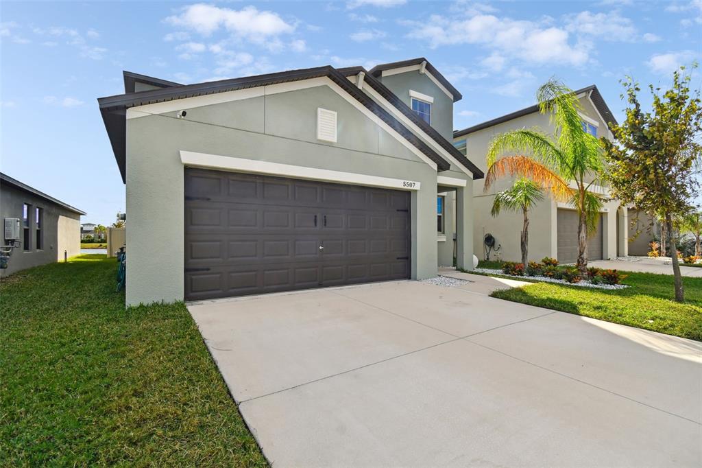A two-story suburban house with a light green exterior and a dark brown garage door — 5507 RAINWOOD MEADOWS DRIVE, APOLLO BEACH, FL