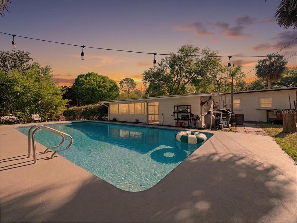 A backyard swimming pool with a concrete deck and string lights at sunset — 106 E JINKINS CIRCLE, SANFORD, FL