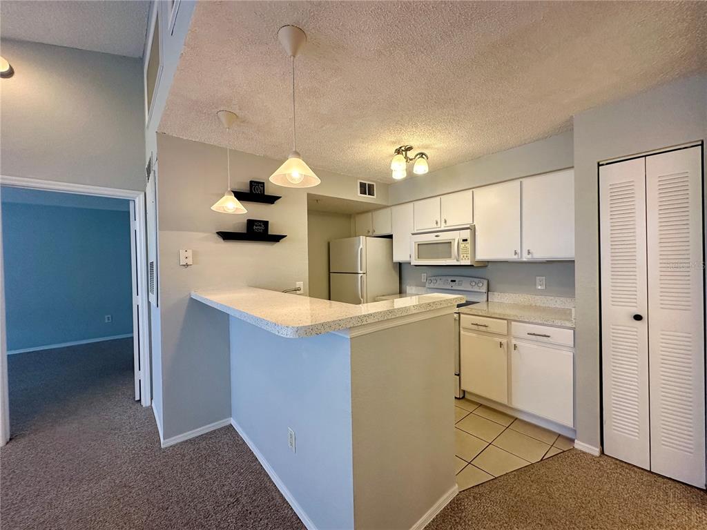 A kitchen with white cabinets, a breakfast bar, and light-colored countertops opens to a carpeted room — 2212 GRAND CAYMAN COURT UNIT 1633, KISSIMMEE, FL