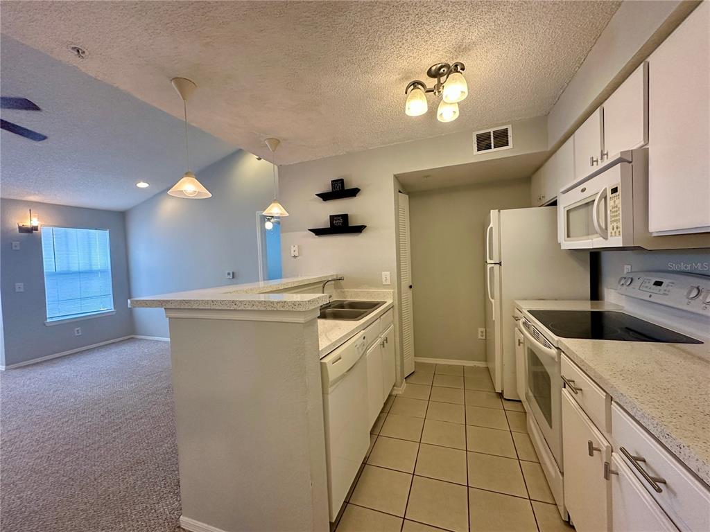 A kitchen with white cabinets, tile flooring, and a breakfast bar overlooking a carpeted room — 2212 GRAND CAYMAN COURT UNIT 1633, KISSIMMEE, FL