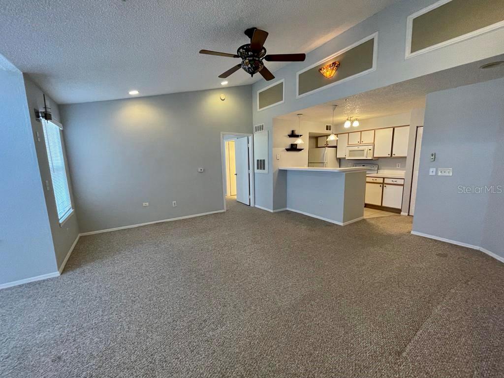 A carpeted living room with a vaulted ceiling and ceiling fan opens to a kitchen — 2212 GRAND CAYMAN COURT UNIT 1633, KISSIMMEE, FL