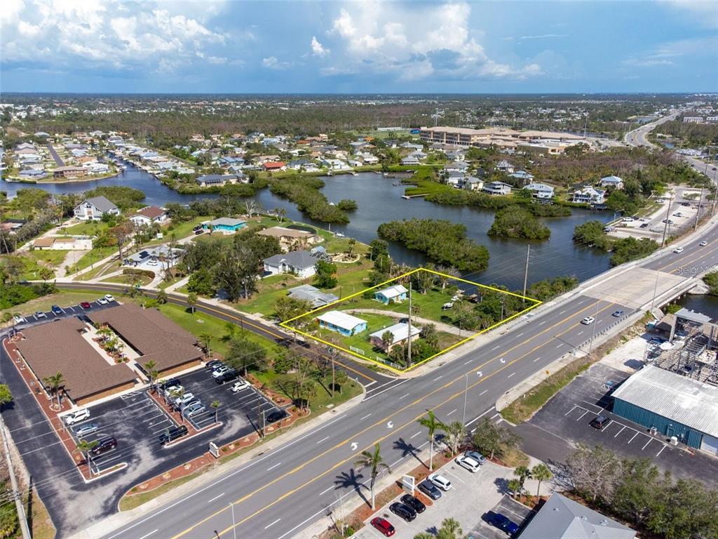 An aerial view shows a yellow-outlined lot containing two small houses near a road — 1695 MANOR ROAD, ENGLEWOOD, FL
