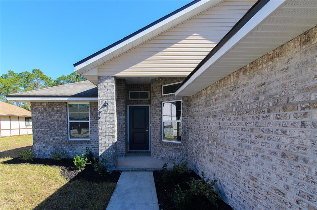 A brick house exterior features a covered entryway, a dark front door, and beige siding — 14 WENDOVER LANE, PALM COAST, FL