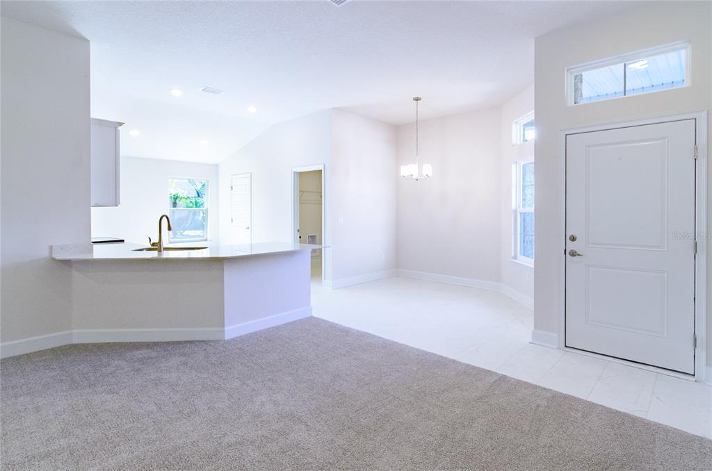 An open-concept living area features carpeted flooring, a kitchen breakfast bar, and a dining space — 14 WENDOVER LANE, PALM COAST, FL